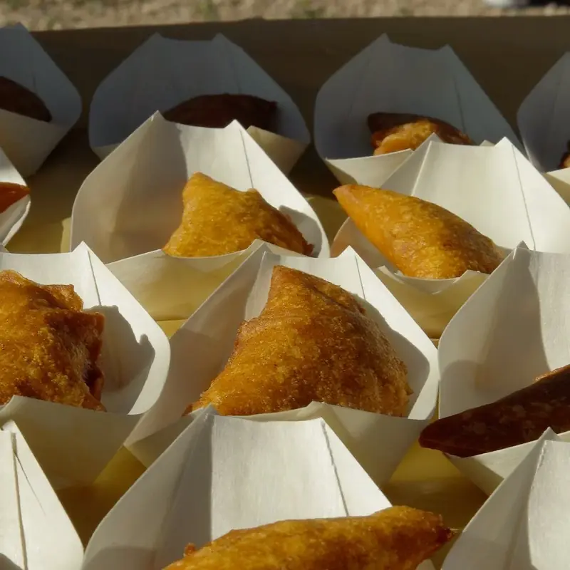 Golden fried half-moon turnovers, each in a white paper boat, lined up in a box outdoors